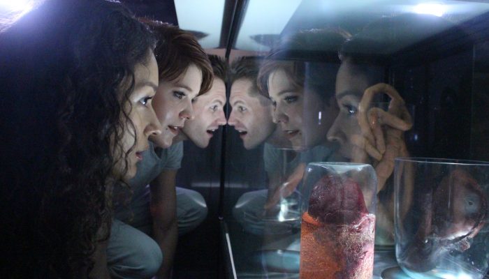 Three friends in the alien encounter escape room look into a mysterious glass container